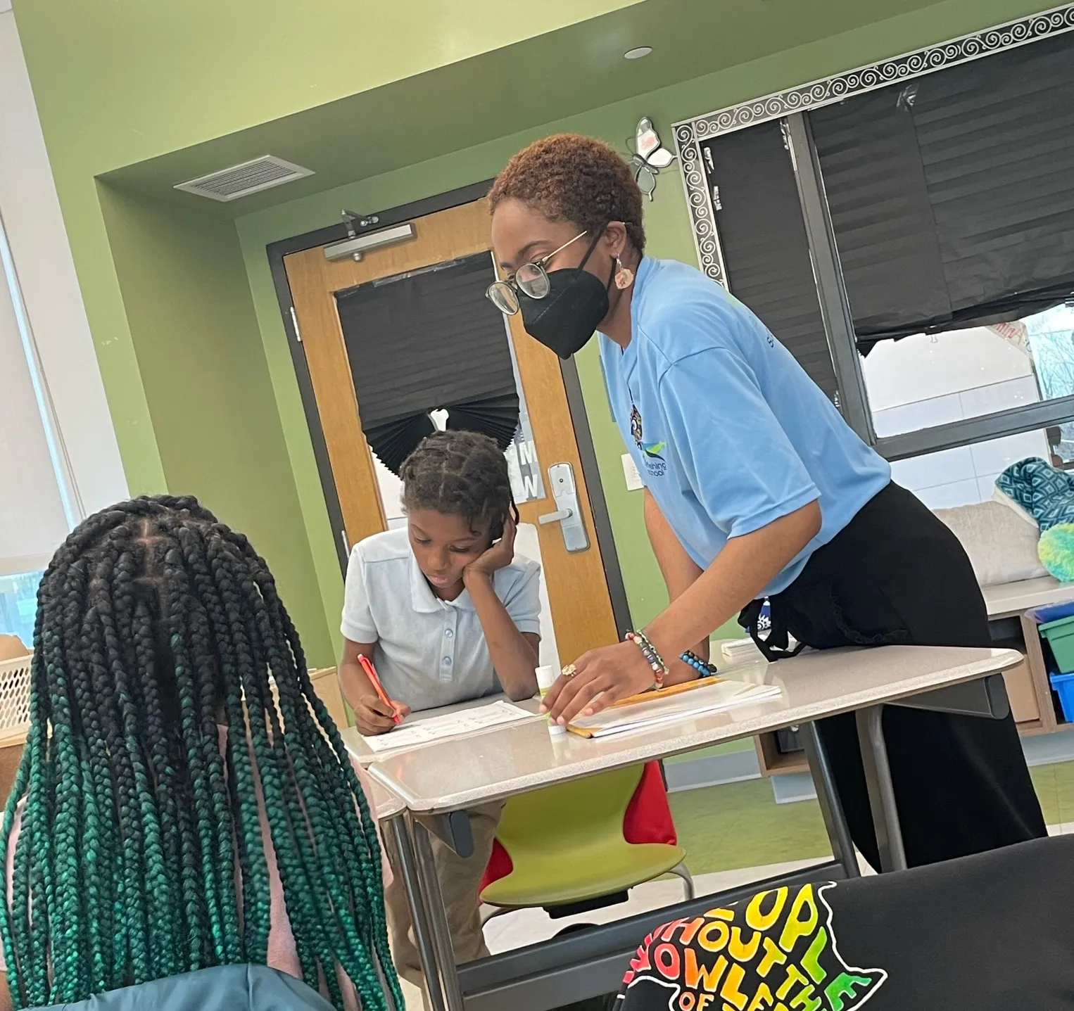 Masked tutor leaning across a table to help seated students