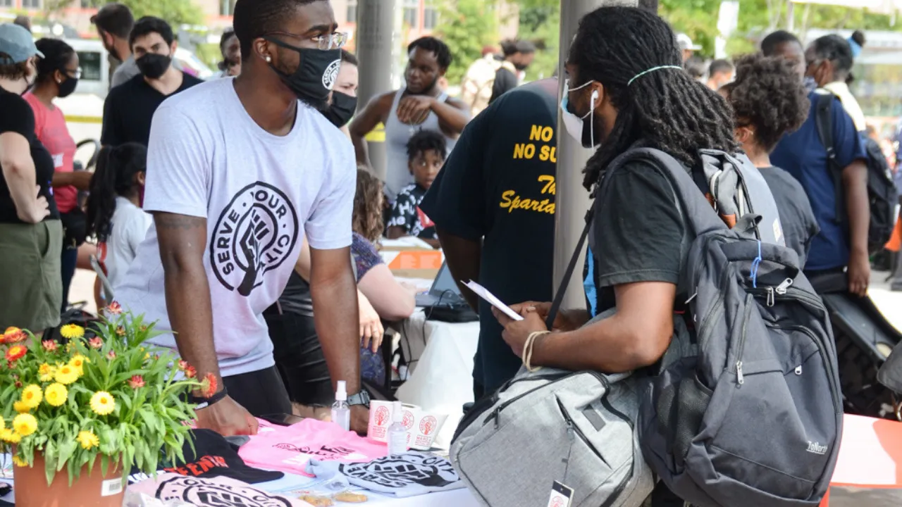 People gathered around a flower and supply table at an outdoor community event