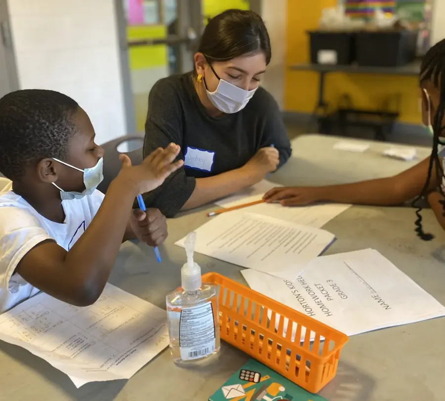 Masked woman helping a student at a table