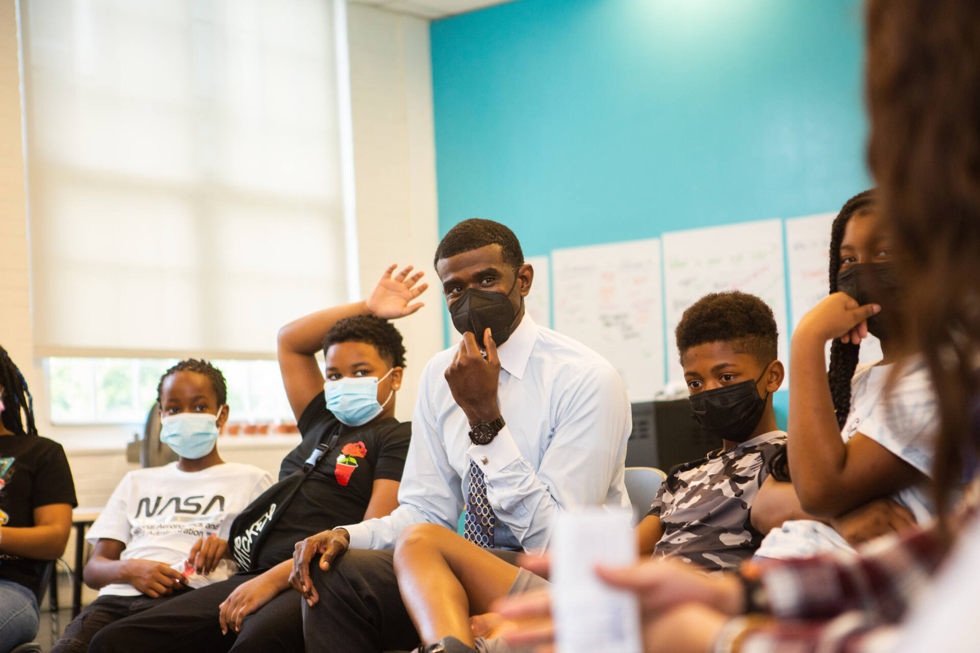 Students sit in seats around tutor in a classroom