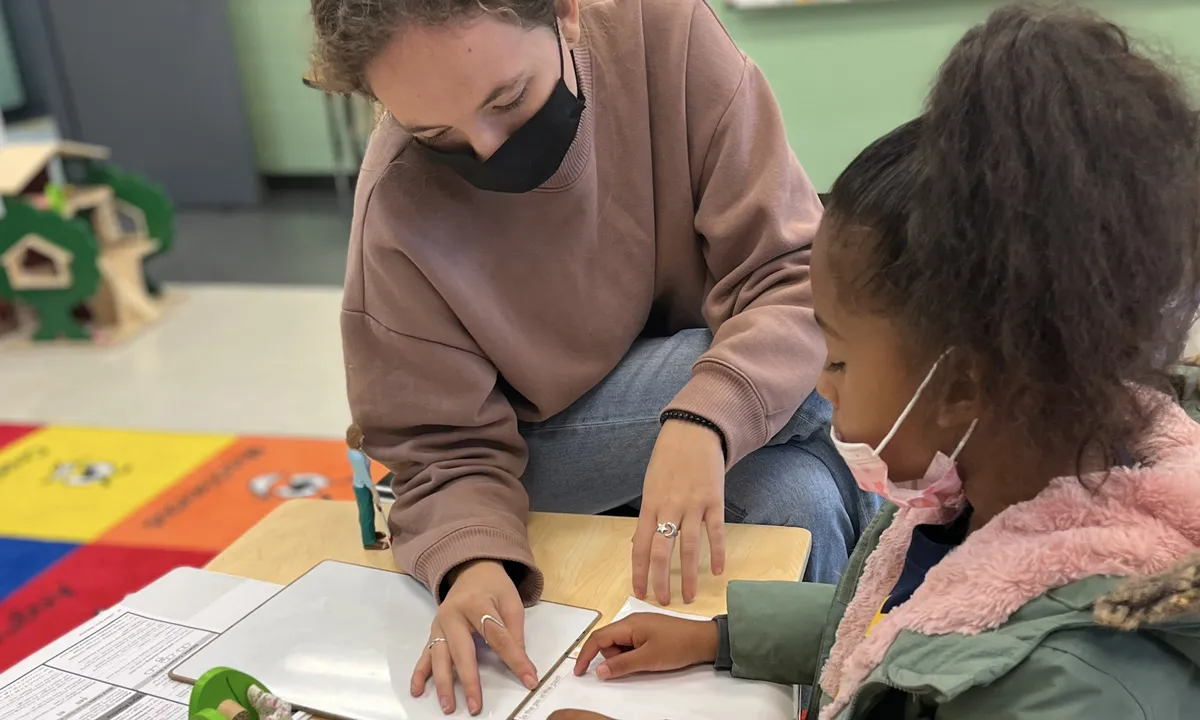 Adult helping two girls use colorful blocks at a table