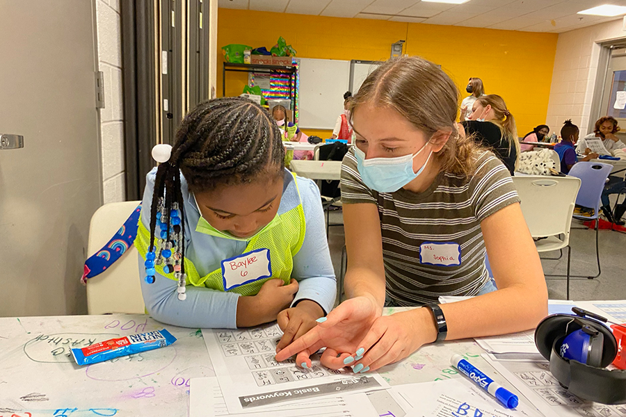 Tutor points out a word on a worksheet while the student looks on.