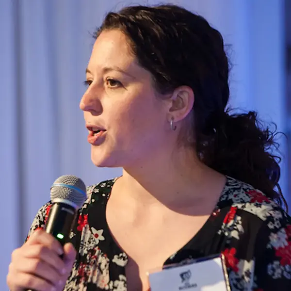 Woman speaking into a handheld microphone at an indoor event