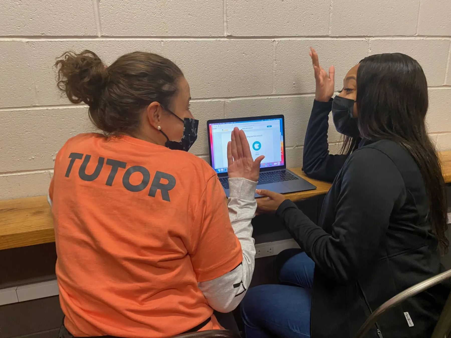 Tutor in an orange shirt and seated student pointing at a laptop screen