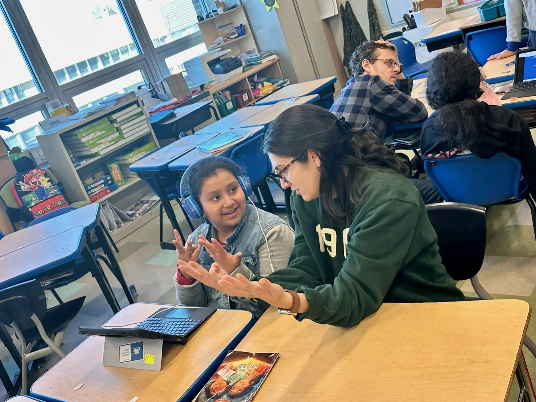 Woman gesturing while helping a student at a laptop in a classroom