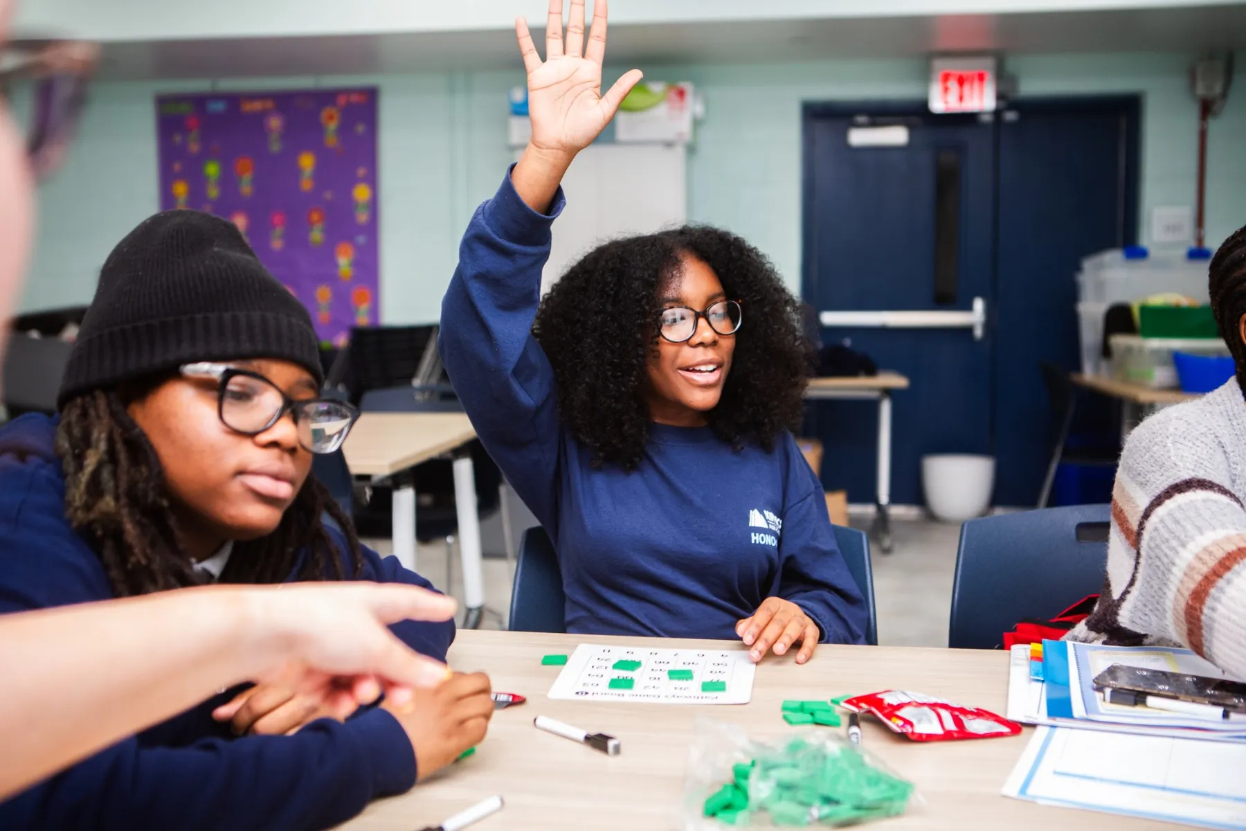 Three students at a table while one raises her hand