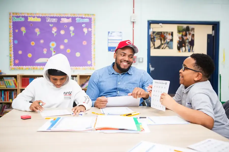 Man in a red cap helping two students at a table