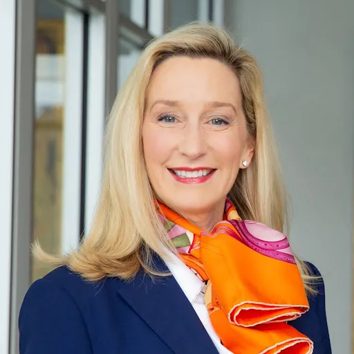 Portrait of a blonde woman wearing a navy blazer and bright orange scarf
