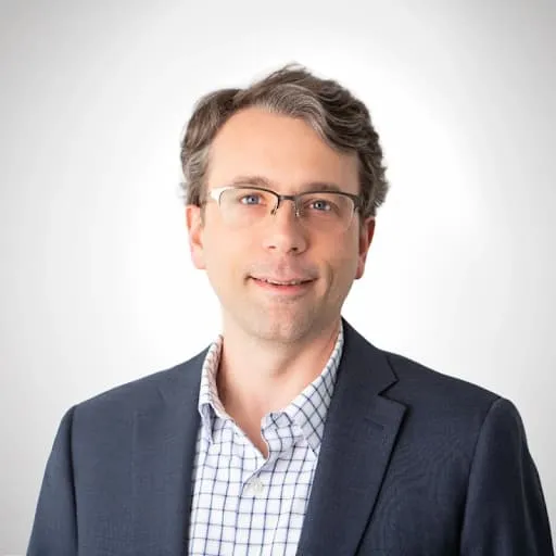 Man with glasses wearing a dark blazer and checked shirt