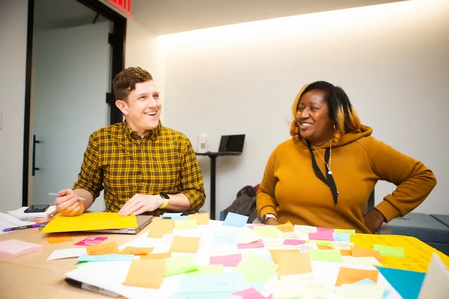 Two women smiling at each other across a table covered with colorful notes