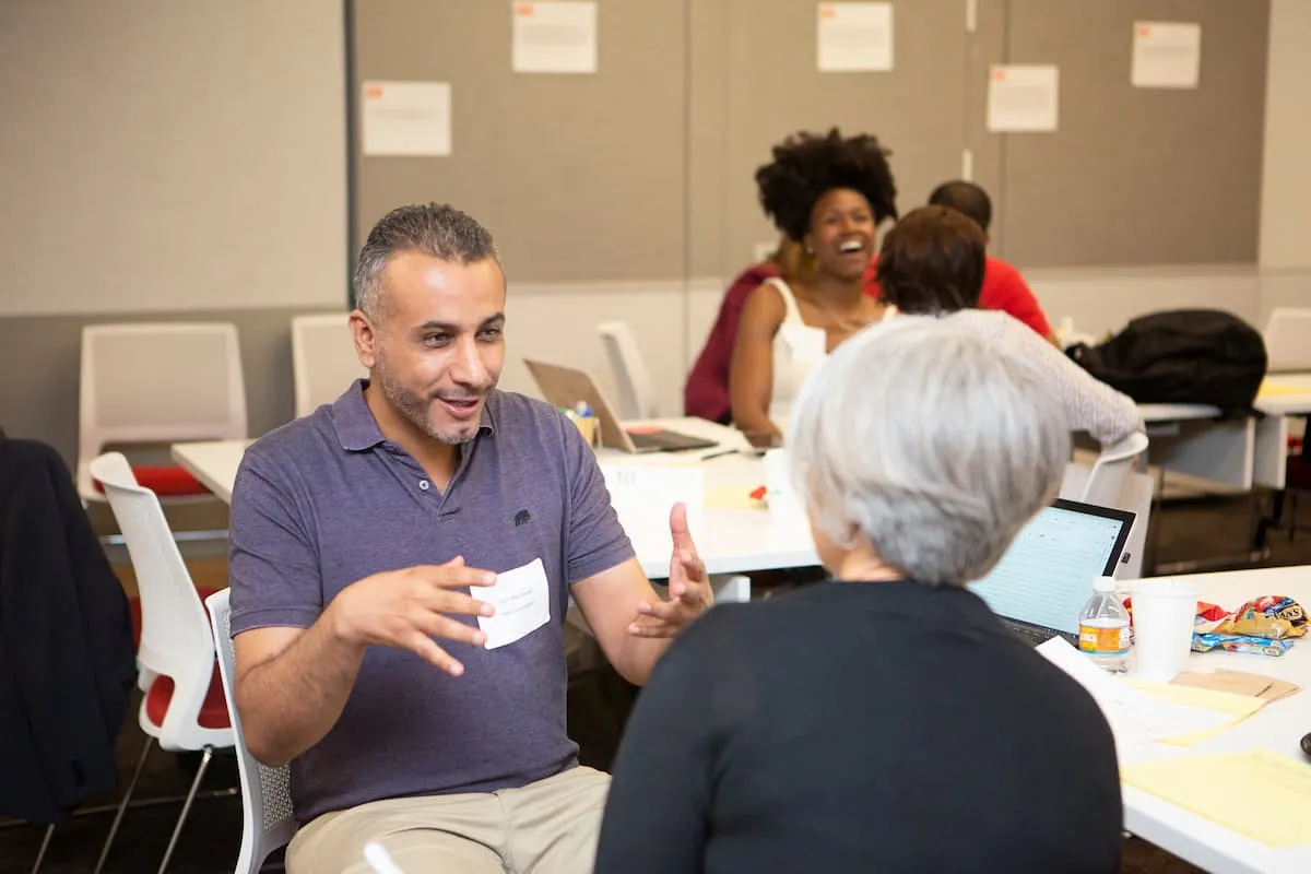 Man gesturing while speaking with a seated woman at a workshop