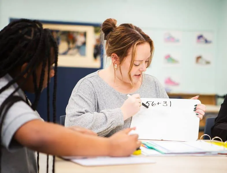 Woman writing on a small whiteboard while seated with students