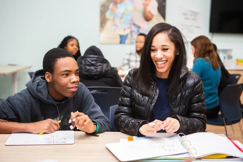 Woman smiling while seated beside a student with open notebooks