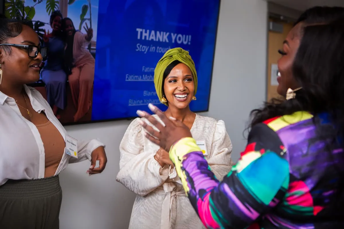 Woman in a yellow headwrap talking with two other women at an indoor event