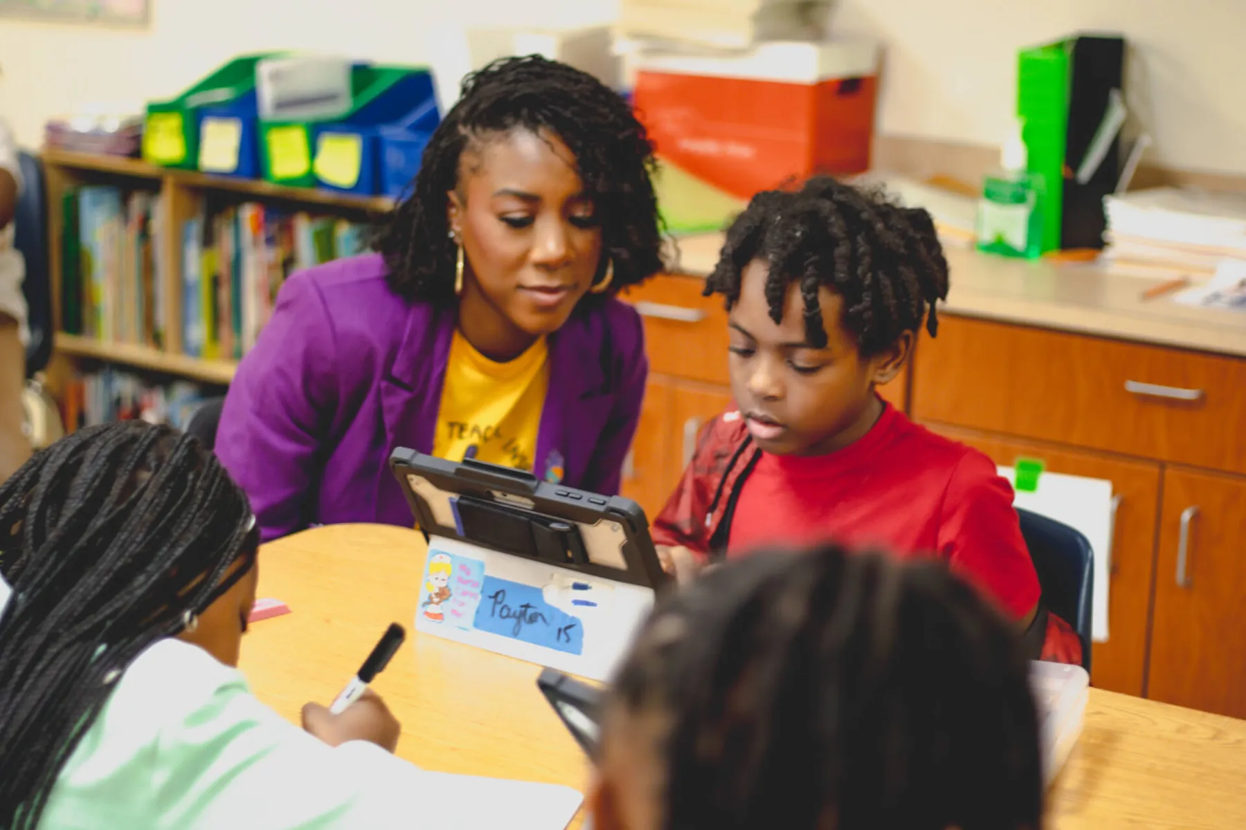 Woman helping children use a tablet at a classroom table