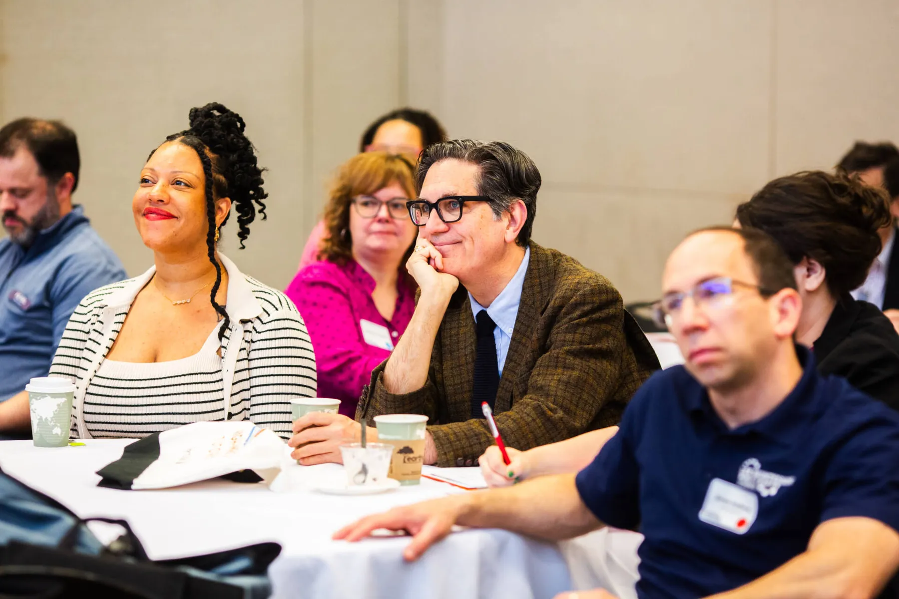 Adults seated at a conference table listening and taking notes