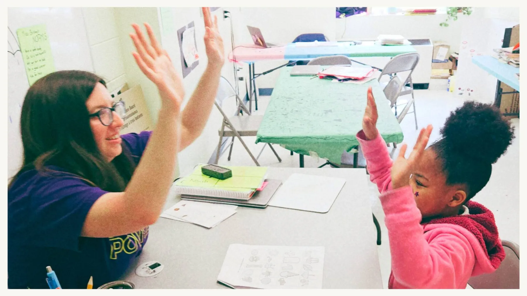Woman and girl raising their hands for a high-five across a table - CitySchools Collaborative Kid Power, High-Impact Tutoring